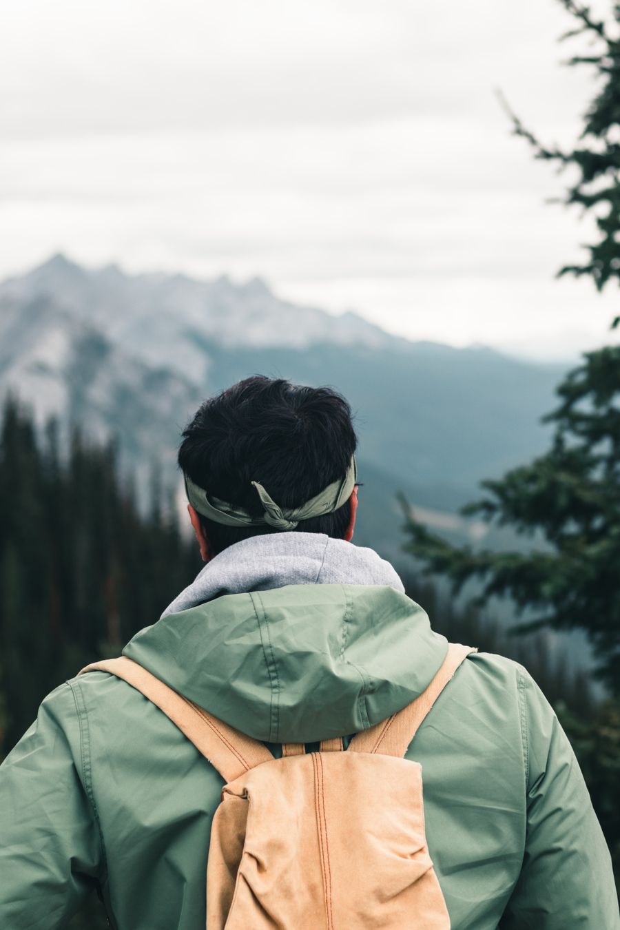a man in green jacket carrying a brown backpack — Support: ルーフトップでチェックイン：搭乗券もホテルの鍵も、すべてスマホに。