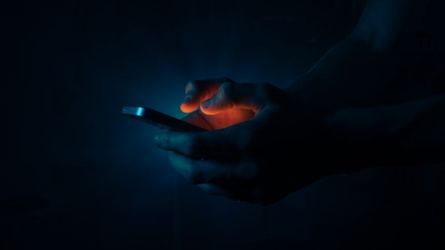 man holding a mobile phone in the dark — 決済画面に番号オプションを明示 — 事前チェックの罠なし。