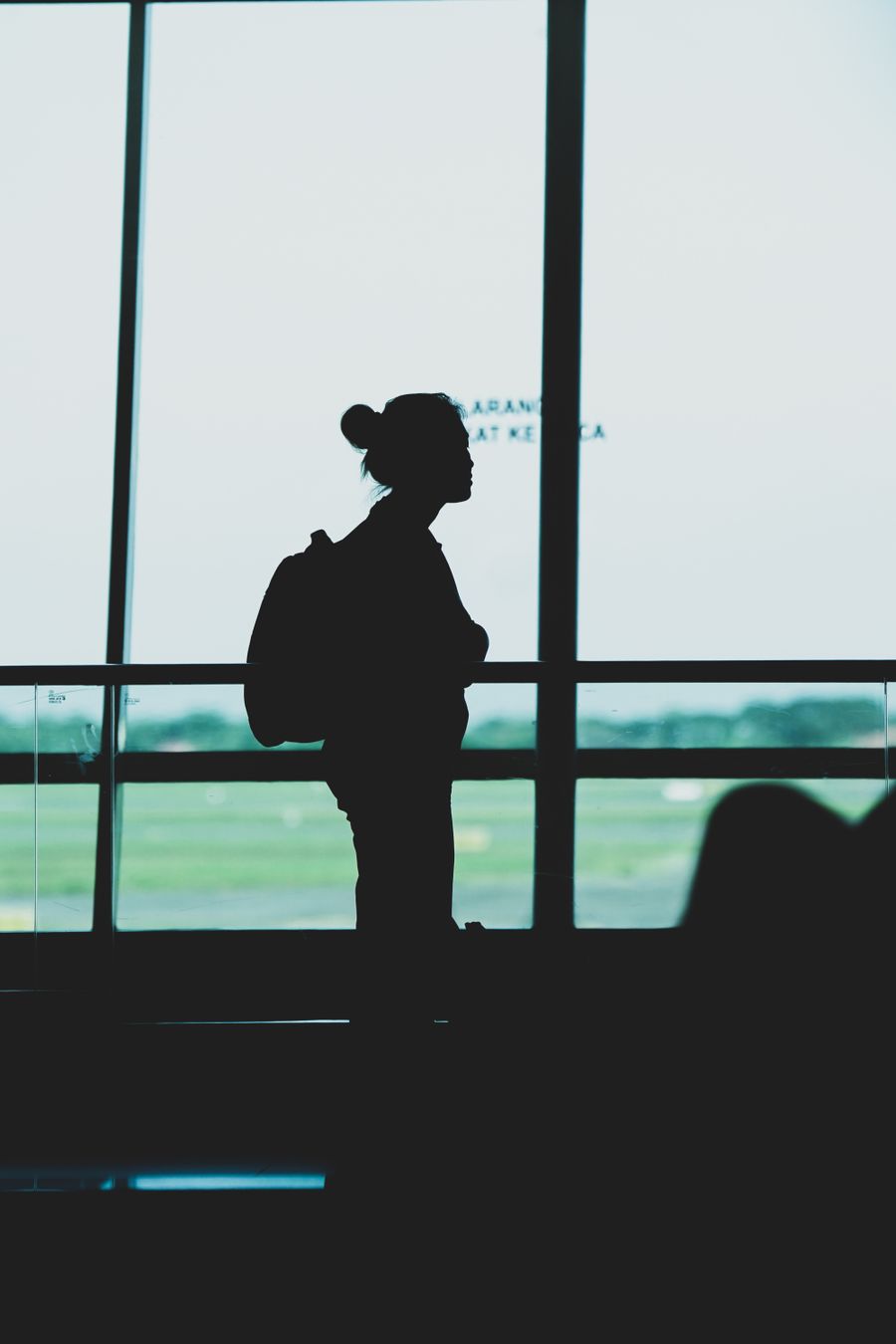 silhouette of a woman with a backpack standing at an airport terminal — 雨の日のバックアップ計画：ホステルのベッドから屋内スポットをリサーチ。