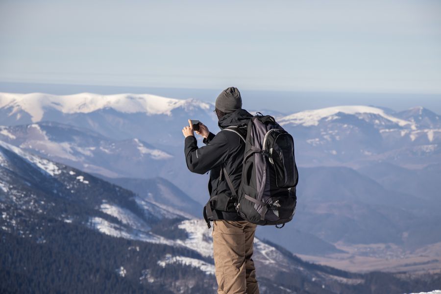 A person capturing the stunning view of snowy mountains with a smartphone. — 電波フルで港を望む：旅行者が実際に行く場所でのカバレッジ。