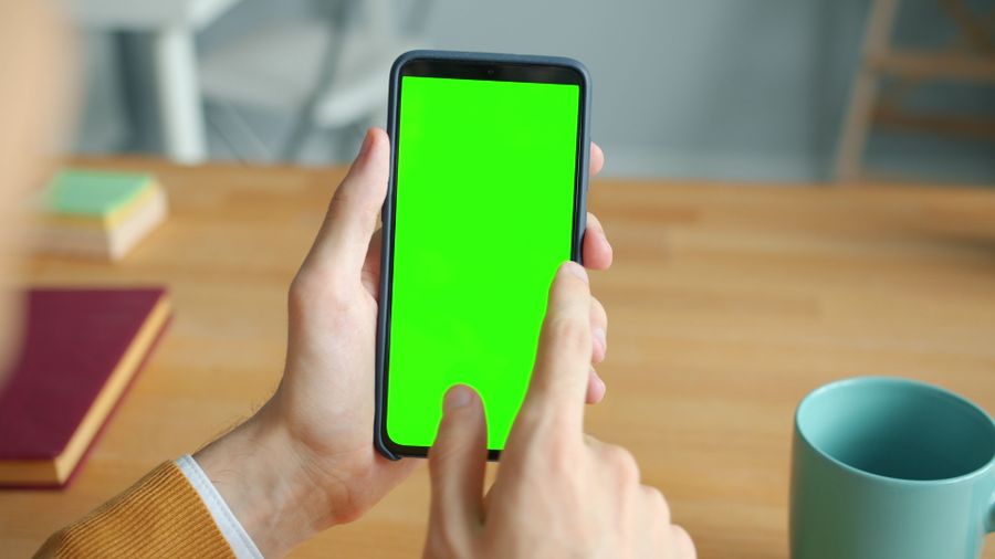 person using smartphone with green screen at desk — The commute, handled: podcasts downloaded, messages sent, no dead zones.