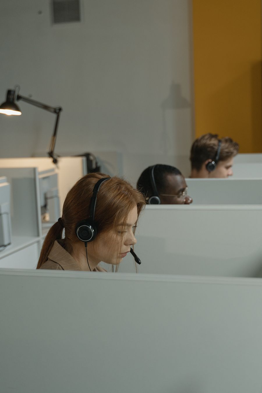 a woman with headset inside a gray cubicle — The rental desk handshake: confirmation email open, license photo ready.