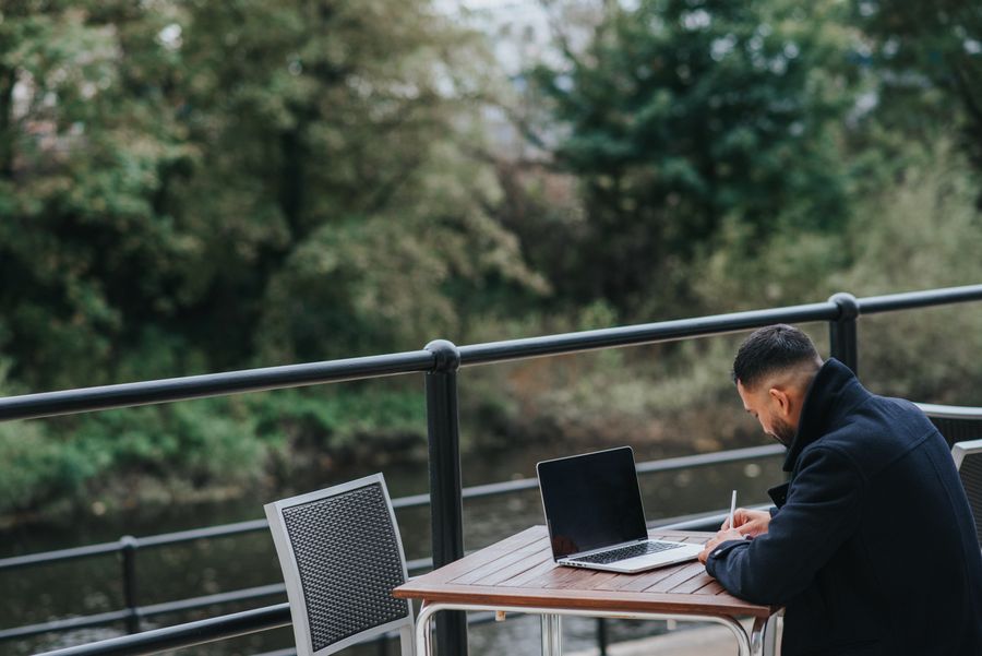 anonymous ethnic worker writing near laptop on cafe terrace — Device Compatibility Checker links every answer onward — usually the plan it recommends.