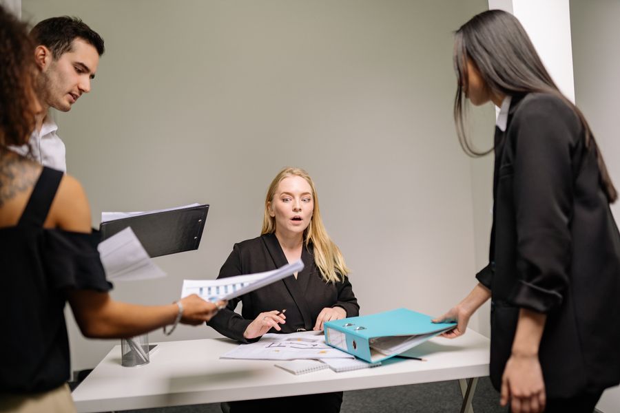 a woman in black blazer sitting at the desk with documents — 書類のやり取りなしの国境越え:身分証の写真はスマホに保存。