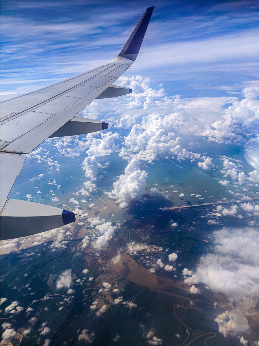 photo of an airplane wing over white clouds — 両替所はスキップ：スマホが実勢レートで支払います。